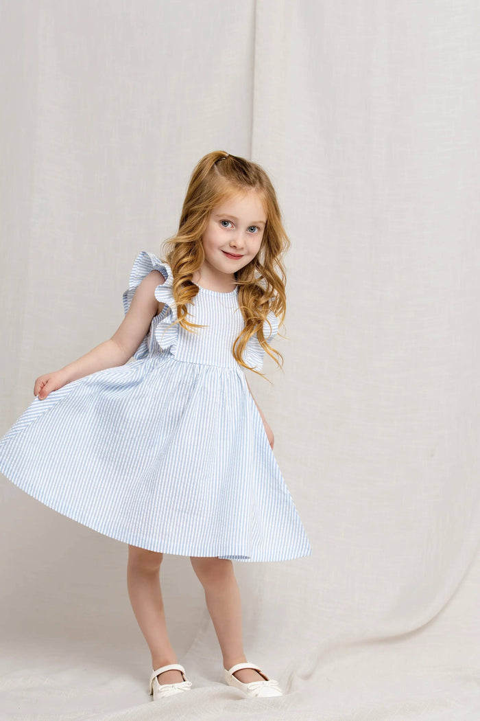Young girl wearing a light blue and white striped dress against a plain background