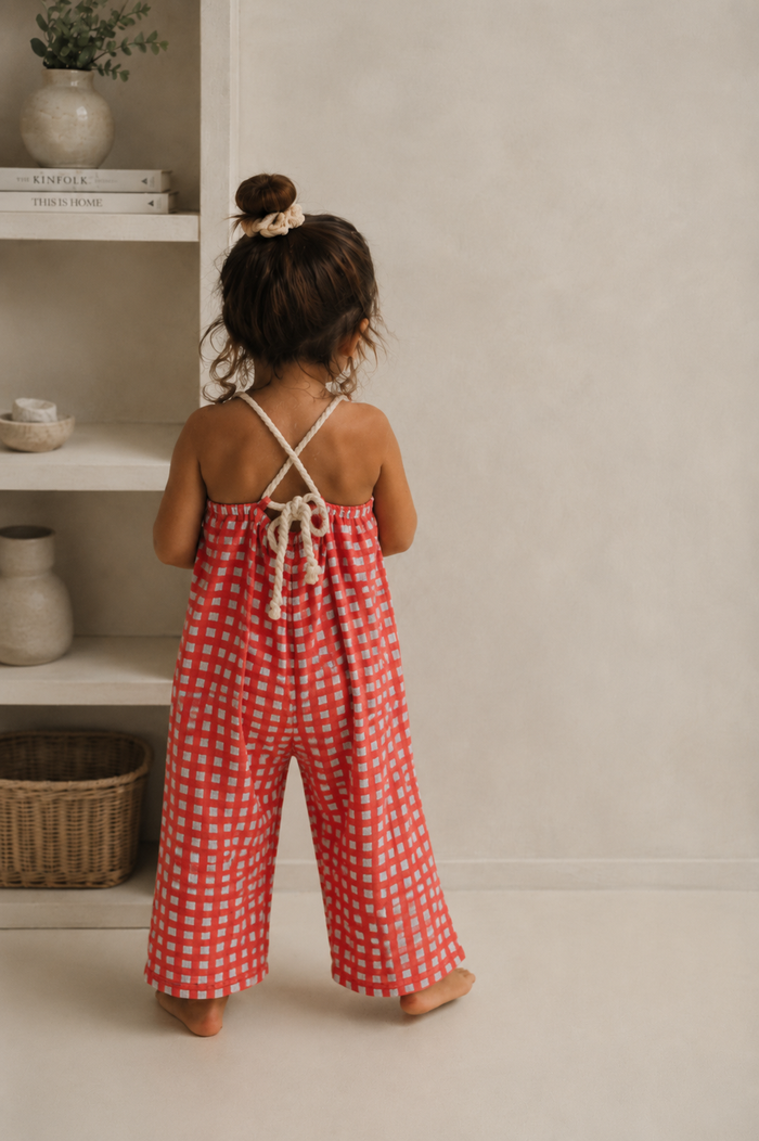 Child wearing a red checkered jumpsuit standing in a room with shelves and decor.