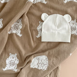 White baby hat and pink teething ring on a brown fabric background with lace patterns