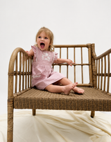 Child in a pink dress sitting on a wicker chair with a white background