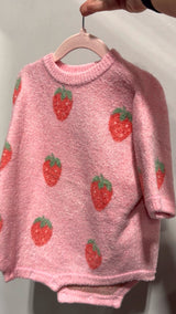 Pink sweater with strawberry pattern on a hanger against a neutral background