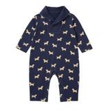 A baby long-sleeve one-piece romper in navy blue with an allover print of small tan and cream dachshund dogs, featuring a mock collar and snap-button placket, shown flat against a light cream background.