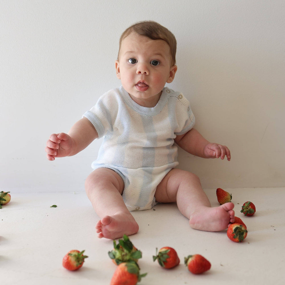 Baby sitting on a white surface with strawberries around