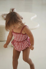Child wearing a red and white checkered dress on a light background