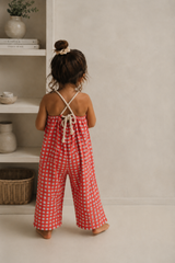 Child wearing a red checkered jumpsuit standing in a room with shelves and decor.