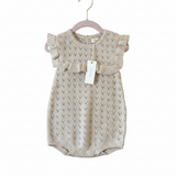 Knitted baby romper with ruffled shoulders on a textured surface