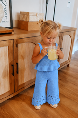 Child in a blue outfit drinking from a straw in a room with wooden furniture.