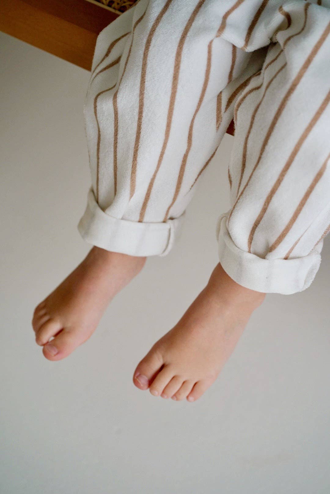 Child's feet wearing white pants with brown stripes on a plain background