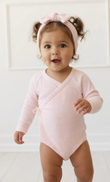 Baby wearing a pink long-sleeve bodysuit and headband against a white background