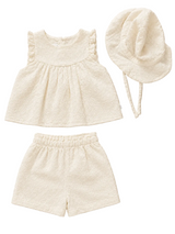 Set of cream-colored baby outfit with top, shorts, and hat on a beige background