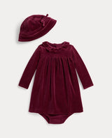 A baby clothing set featuring a long-sleeve dress and a matching bonnet in deep burgundy velvet, displayed on a light gray background.
