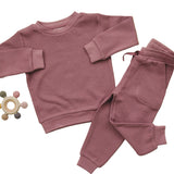 Pink children's sweatshirt and pants set on a beige background with a baby toy.
