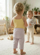 Two young children standing in a room with light-colored carpet and furniture.